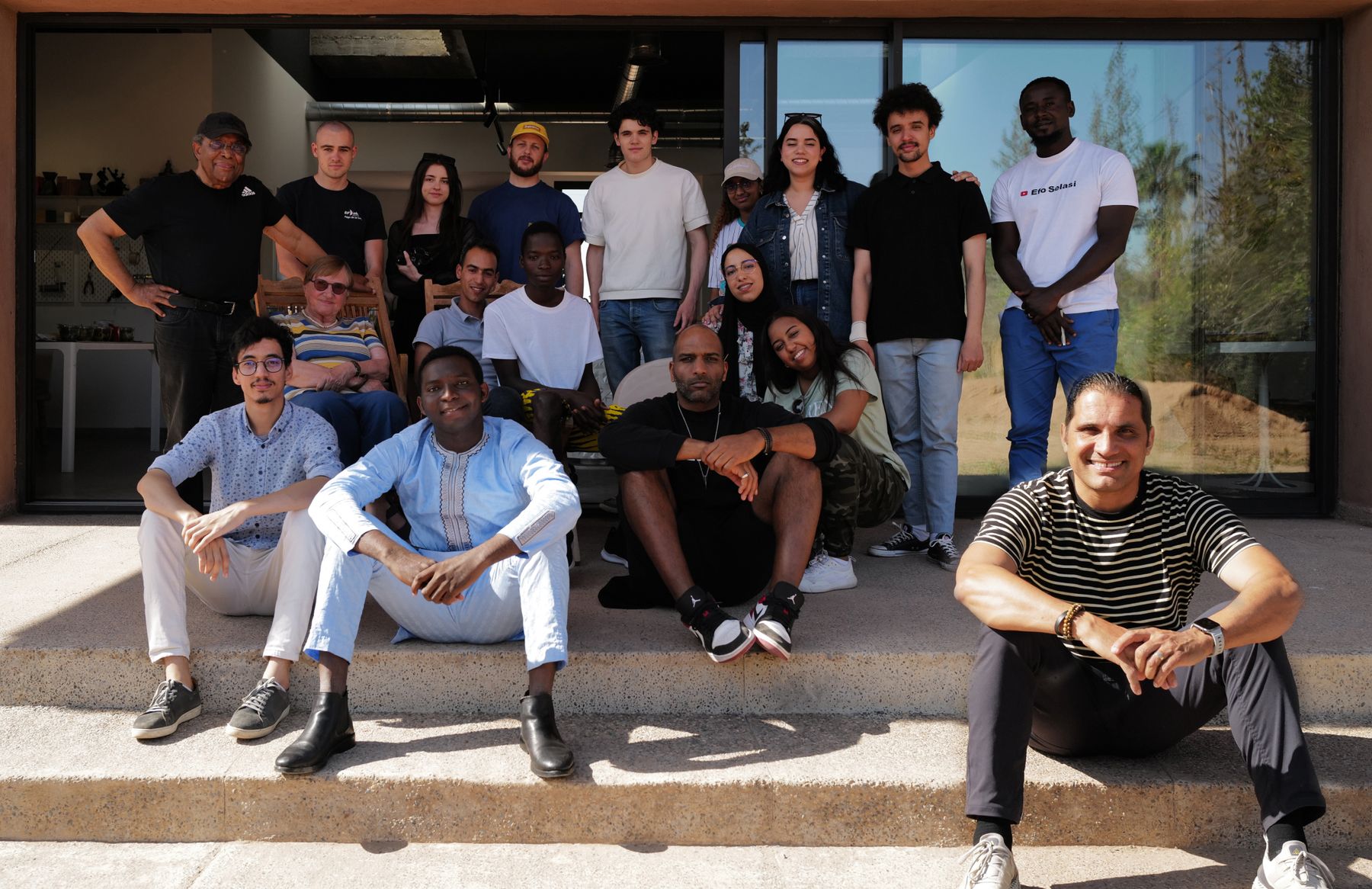 A group of participants and mentors sitting on the steps outside Younes Duret Studio