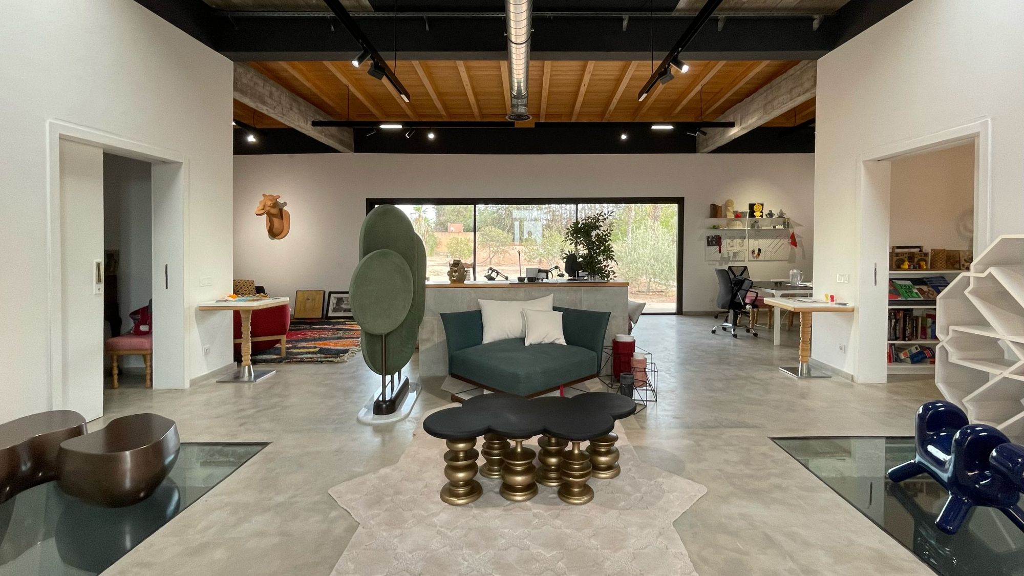The main hall of Younes Duret Studio: concrete floor, timber ceiling, sculptural furniture and a window onto the palm grove