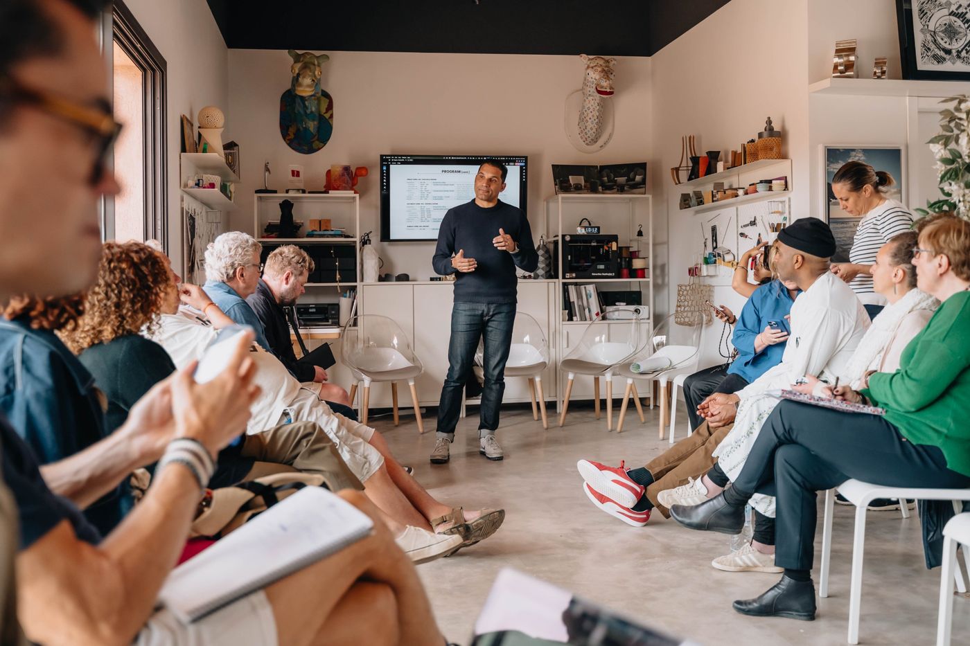 A group seated in a circle during a session at the studio, with a speaker at the screen